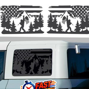Puede incluir: Calcomanías negras de vinilo para ventanas de coche con una escena de montaña y una figura ondeando una bandera estadounidense. El diseño incluye una bandera estrellada, montañas y pinos. Las calcomanías se muestran en un vehículo.