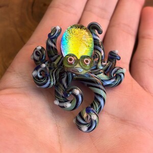 May include: A colorful glass octopus figurine with a yellow and green iridescent head and striped tentacles in shades of blue, green, and white. The octopus has large, round eyes and is a unique decorative item.