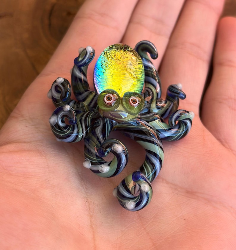 May include: A colorful glass octopus figurine with a yellow and green iridescent head and striped tentacles in shades of blue, green, and white. The octopus has large, round eyes and is a unique decorative item.