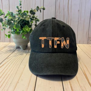 May include: A black baseball cap with a white brim and the text "TTFN" in orange letters.