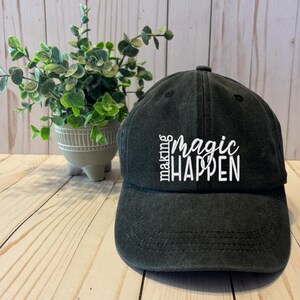 May include: A black baseball cap with white embroidery that reads "Making magic happen".