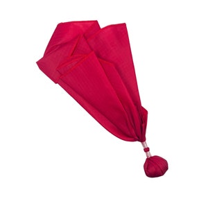 Puede incluir: Una bolsa de tela roja con cierre de cordón. La bolsa está doblada y atada en la parte superior, creando una forma de borla.