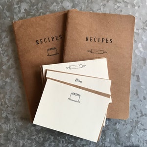 May include: Two brown recipe notebooks with the word "RECIPES" printed on the front. One notebook has a cake icon and the other has a rolling pin icon. There are also four blank recipe cards with cake and rolling pin icons.