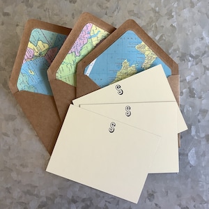 May include: Three cream-colored envelopes with a brown paper outer layer. Each envelope has a map of the world printed on the inside and a black letter 'S' printed on the front.