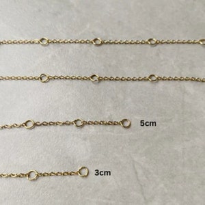 May include: Four gold chain extenders of different lengths: 3 cm, 5 cm, 8 cm, and 10 cm. Each extender has a lobster clasp on one end and a jump ring on the other.