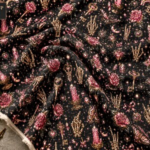 Peut inclure: Tissu noir avec un motif répétitif de roses roses, de mains squelettiques dorées, de clés ornées, de bougies roses allumées dans des bougeoirs, de petits nœuds et de croissants de lune, parsemé de minuscules étoiles blanches.