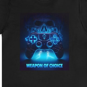 Könnte beinhalten: Schwarzes T-Shirt mit einer blauen und weißen Grafik einer Videospielkonsole mit einem Schädel dahinter. Der Text "WEAPON OF CHOICE" befindet sich unter der Konsole.