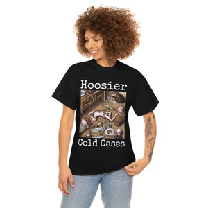 May include: Black t-shirt with a white graphic print of a painting. The painting depicts a group of people in a room with a wooden floor. The text "Hoosier Cold Cases" is printed below the painting.