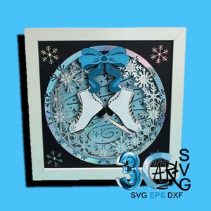 May include: A framed paper art piece with a winter theme. It features white ice skates, a blue bow, and silver snowflakes in a circular design. The artwork is set against a black background within a white frame. The image includes the text "3D SVG" and "SVG EPS DXF".