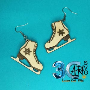 May include: A pair of wooden ice skate earrings. Each earring features a light-colored skate with a dark brown blade and a snowflake design. The earrings hang from silver-colored hooks. The background is a solid teal color.