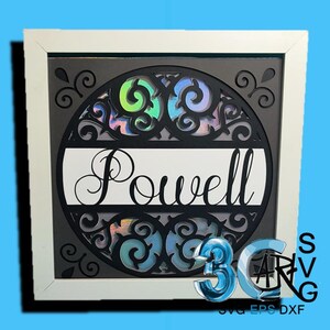 May include: Framed wall art displaying the name "Powell" in a cursive font. The design incorporates a black, laser-cut circular pattern with iridescent highlights, set against a dark grey backdrop, and framed in white.