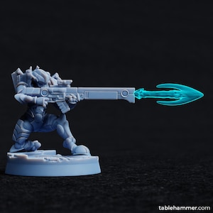 Puede incluir: Una miniatura de plástico gris de un soldado futurista sosteniendo un rifle con un rayo de energía azul que sale del extremo del cañón.