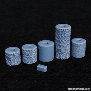 May include: Six different gray textured cylindrical shapes with various patterns. The cylinders are arranged in a row on a black surface. The smallest cylinder is on the left and the largest cylinder is on the right. The cylinders are all about 2 inches tall.
