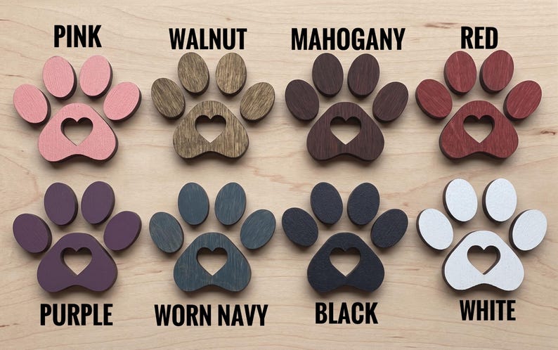 May include: Eight wooden paw print cutouts with heart-shaped centers, arranged in two rows. Colors include pink, walnut, mahogany, red, purple, worn navy, black, and white. Each paw print is labeled with its corresponding color name in black text.
