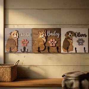 May include: Three rectangular wooden wall-mounted hook racks featuring laser-cut dog silhouettes, paw prints, and names. The left board is light blue with a bulldog named Churchill, the center is brown with a corgi named Bailey, and the right is white with a beagle named Oliver.