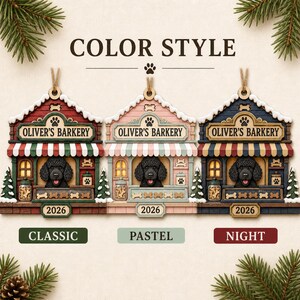 May include: Three house-shaped ornaments labeled OLIVER'S BARKERY and 2026, featuring a black poodle in a shop window. The versions are Classic in red and green, Pastel in pink and light blue, and Night in dark blue and red, all with hanging twine.