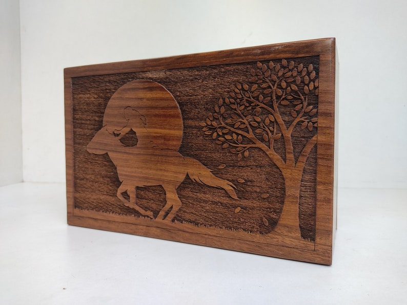 May include: A wooden box with a carved design of a horse running through a moonlit forest. The horse is silhouetted against a full moon, and a tree with leaves is in the background.