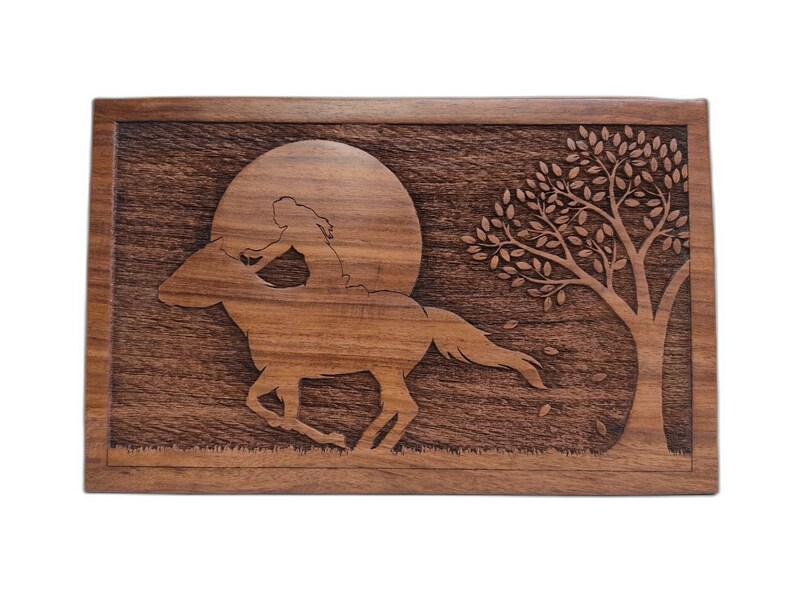 May include: A wooden box with a carved design of a woman riding a horse under a full moon with a tree in the background.