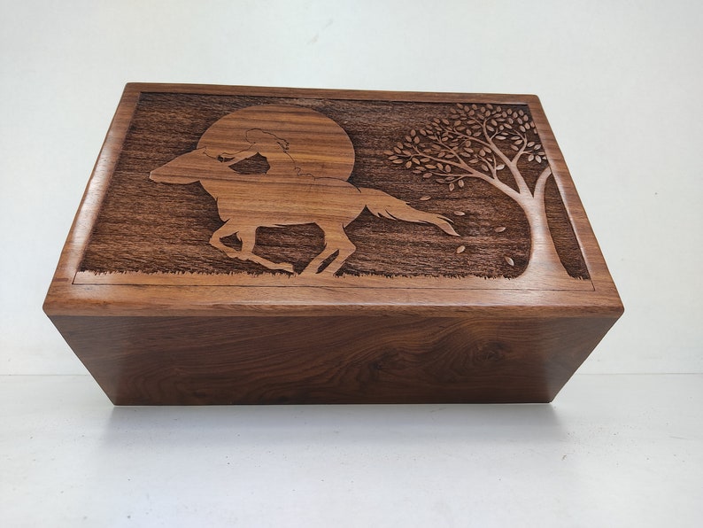 May include: A wooden box with a carved design of a horse and rider galloping under a full moon with a tree in the background.