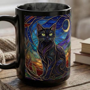 May include: A black ceramic mug featuring a vibrant stained glass style illustration of a black cat with bright green eyes. The background depicts a swirling night sky with a crescent moon in shades of deep blue, purple, and warm orange tones.