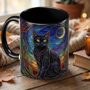 May include: Black ceramic mug with a stained-glass design featuring a black cat with green eyes, a crescent moon, and stars. The mug has a black handle and interior. The background includes shades of blue, purple, and gold.