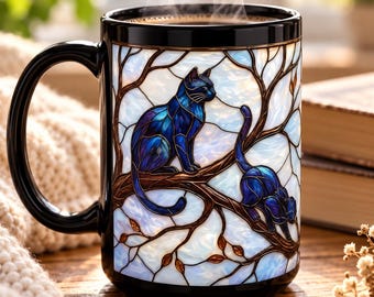 Può includere: Una tazza in ceramica nera con un design in stile vetrata raffigurante due gatti blu scuro appollaiati su rami d'albero marroni su uno sfondo azzurro e bianco. Il vapore sale dalla parte superiore della tazza, dotata di un manico nero.