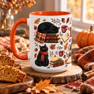 May include: A white ceramic mug with an orange handle and interior, featuring a repeating pattern of black cats, stacks of books, autumn leaves, acorns, berries, pumpkins, and small mugs, all rendered in a detailed, colorful illustration style.
