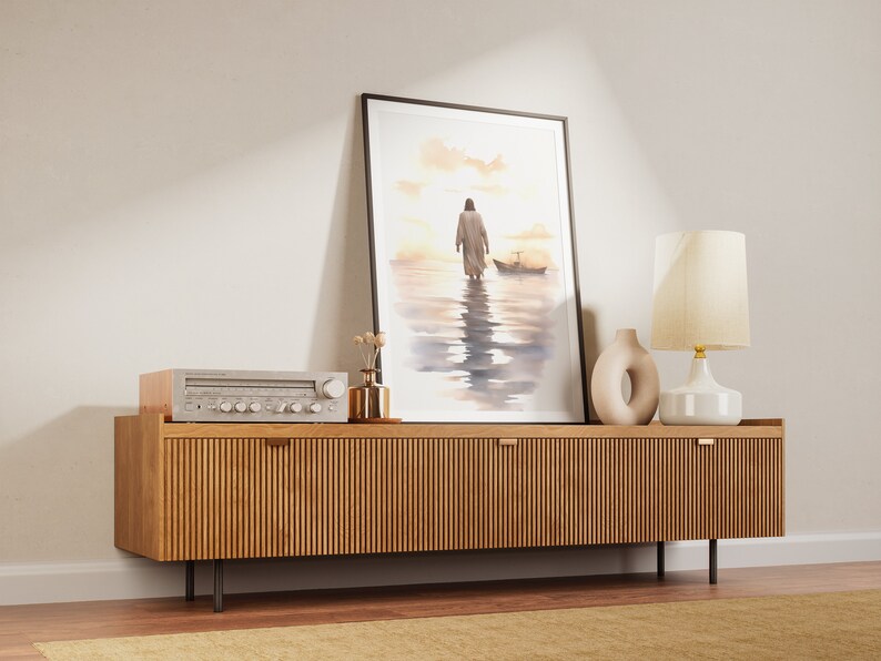 May include: A framed watercolor painting of a person walking on water with a boat in the distance. The painting is hanging on a wall above a wooden cabinet with a stereo and a lamp.