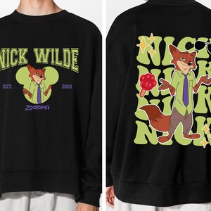 May include: Black sweatshirt featuring a cartoon fox character, Nick Wilde, from Zootopia. The front design includes the text "NICK WILDE" and "EST. 2016 ZOOTOPIA". The back design shows the fox with sunglasses and the name "NICK" repeated.