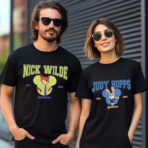 May include: Black t-shirts featuring characters from the movie Zootopia. One shirt displays "Nick Wilde" with a fox graphic, the other "Judy Hopps" with a bunny graphic. Both shirts have the text "Est. 2016" and "Zootopia".