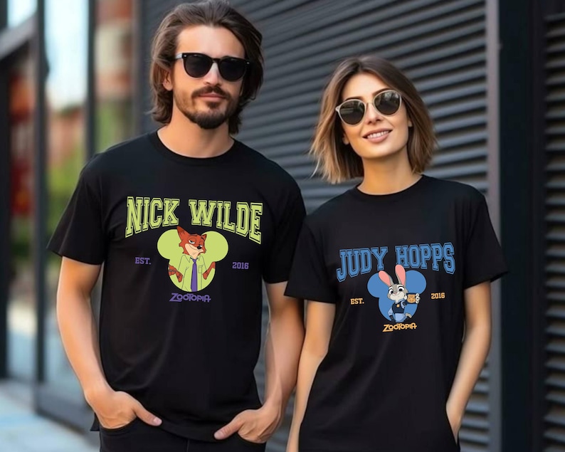May include: Black t-shirts featuring characters from the movie Zootopia. One shirt displays "Nick Wilde" with a fox graphic, the other "Judy Hopps" with a bunny graphic. Both shirts have the text "Est. 2016" and "Zootopia".