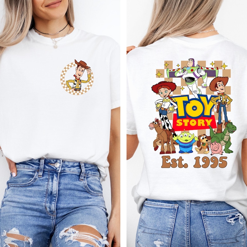 May include: White t-shirt featuring a circular graphic of Woody from Toy Story on the front. The back of the shirt displays a colorful Toy Story graphic with the text "Toy Story" and "Est. 1995".
