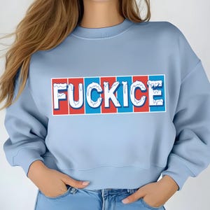 May include: A light blue sweatshirt with the word "FUCKICE" in a white, red, and blue design across the front. The text is in a bold, stylized font, with a frosted effect.
