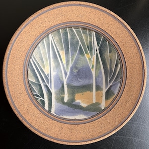 May include: Circular ceramic plate with a painted forest scene. The centre shows white tree trunks against blue, green, and yellow tones. The rim is a speckled tan colour with a darker brown border.