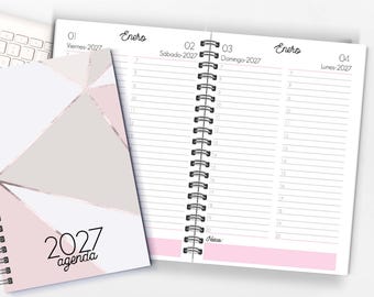 Puede incluir: Una agenda 2027 de espiral con una cubierta geométrica en tonos rosa, blanco y gris. Las páginas abiertas muestran un diseño de planificador diario para enero, con franjas horarias de 7 a 20, incluyendo el texto Enero, Viernes, Sábado, Domingo y Lunes.