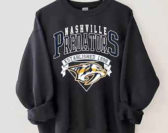 May include: Black sweatshirt with a white and yellow Nashville Predators logo. The logo includes the team name, "Nashville Predators", and the text "Established 1998".