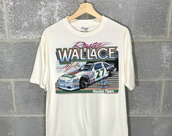 May include: White t-shirt featuring a graphic of Rusty Wallace's #27 Blue Max Racing Team car. The car is green, white and blue with the number 27 on the side. The text "Rusty Wallace" is in a large, bold font above the car.