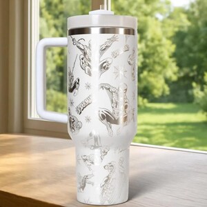 May include: White insulated tumbler with a handle, featuring a repeating pattern of Spider-Man illustrations in silver. The tumbler has a white lid and a silver band at the top. The word "SPIDER-MAN" is also visible.