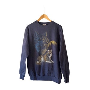 May include: Navy blue sweatshirt with a detailed wolf graphic. The design features two wolves, a full moon, and a forest silhouette. The sweatshirt is displayed on a wooden hanger. The measurements are in centimeters.