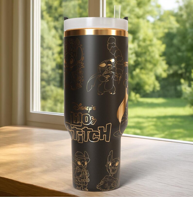 Puede incluir: Vaso negro con ilustraciones doradas de Stitch de Lilo & Stitch de Disney. Tiene una tapa blanca con una banda dorada y una pajita transparente. El texto "Disney's Lilo & Stitch" se muestra en dorado.