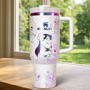 May include: White Stanley tumbler featuring a handle and a screw-on lid. The tumbler is decorated with illustrations of Lilo and Stitch in a colorful, iridescent design. The Stanley logo is also visible.