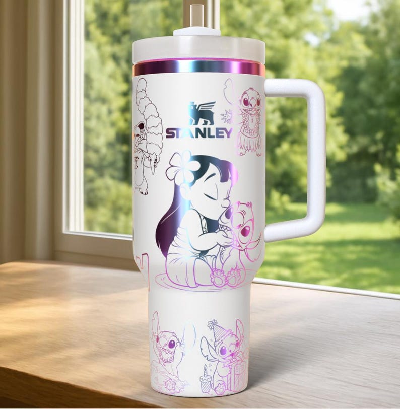 May include: White Stanley tumbler featuring a handle and a screw-on lid. The tumbler is decorated with illustrations of Lilo and Stitch in a colorful, iridescent design. The Stanley logo is also visible.
