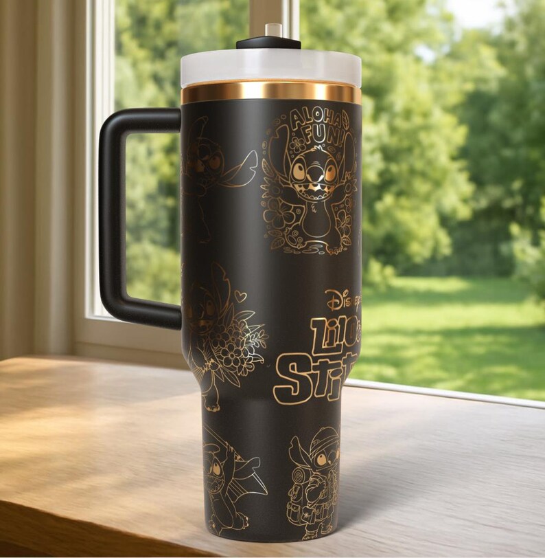 Puede incluir: Taza de viaje negra con ilustraciones doradas de Stitch de Lilo & Stitch. La taza tiene un asa negra, una tapa blanca y una banda dorada. El texto "Aloha Fun" y "Disney Lilo & Stitch" tambi&eacute;n es dorado.