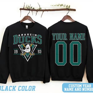 May include: Black sweatshirt with a green and white Anaheim Ducks logo and the text "Anaheim Ducks 19 93". The back of the sweatshirt has the text "Your Name" and a green number "00".