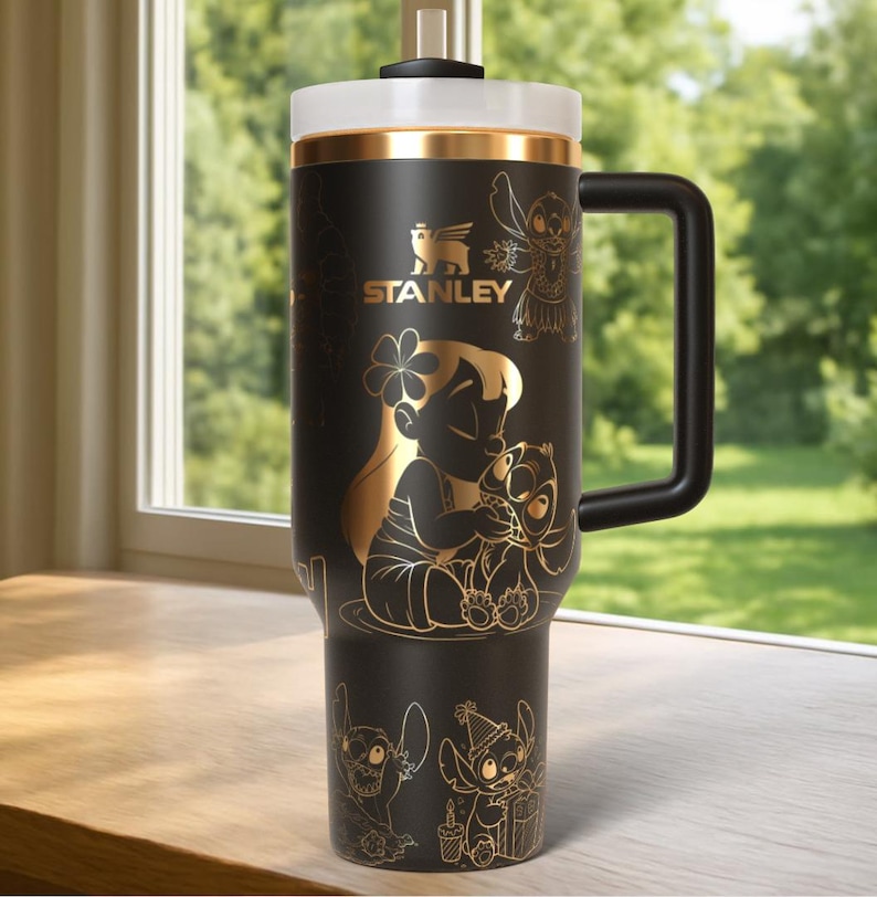 Puede incluir: Vaso Stanley negro con detalles dorados y asa negra. Presenta ilustraciones doradas de personajes de Lilo & Stitch, incluyendo a Lilo y Stitch. El logotipo de Stanley tambi&eacute;n es dorado.