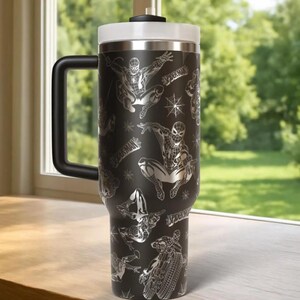 May include: Black travel mug featuring a Spider-Man design. The stainless steel tumbler has a black handle, a white lid, and a silver rim. The design includes Spider-Man in various action poses and the word "Spider-Man".