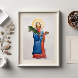 May include: Watercolor painting of a figure in blue and red robes, holding a palm branch and a small plate. The figure has a golden halo and is framed in a white rectangular frame. The artwork is on textured paper.