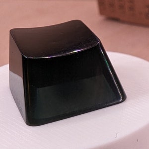 May include: Five black keycaps for a mechanical keyboard. The keycaps are made of a smooth, glossy plastic and have a slightly curved shape. The keycaps are arranged on a white surface.