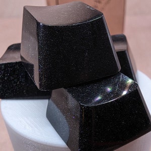 May include: Four black keycaps with a speckled finish. The keycaps are stacked on top of each other.