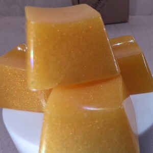 May include: Four square-shaped bars of yellow soap with a glittery finish. The soap is stacked on top of each other.
